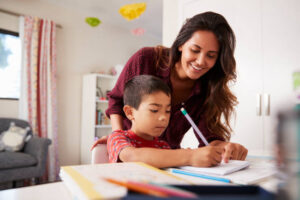Mother Helping Son With Homework Sitting At Desk In Bedroom
